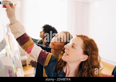 Confident female technicians discussing project over whiteboard by businessman working at creative office Stock Photo