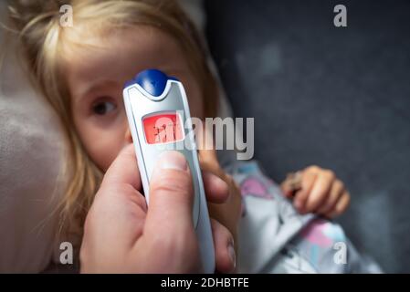 Parent takes temperature for her child with infrared thermometer at home, low-grade fever Stock Photo