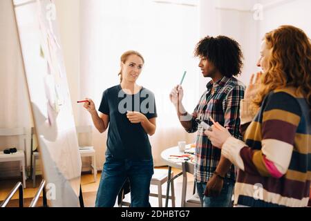 Confident businesswoman discussing project over whiteboard with technicians at creative office Stock Photo