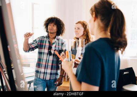 Confident multi-ethnic technicians discussing project over whiteboard at creative office Stock Photo