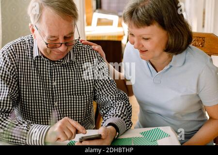 Smiling mature female social worker looking at retired senior man using smart phone in nursing home Stock Photo