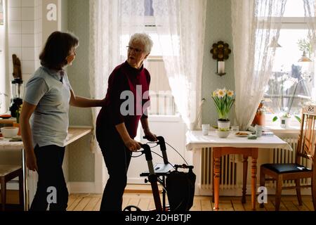 Side view of female healthcare worker supporting elderly woman with rollator in nursing home Stock Photo