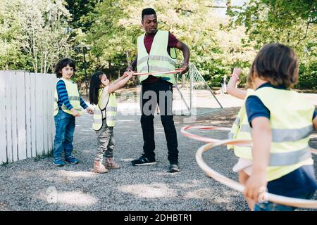 Male teacher and students playing with plastic hoops in playground Stock Photo
