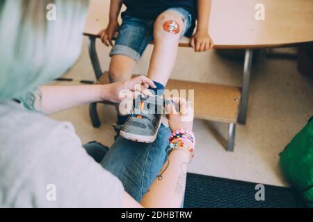 High angle view of female teacher helping boy in wearing shoe at preschool Stock Photo