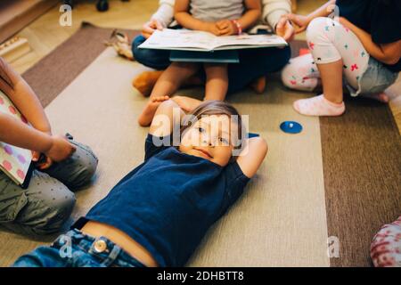 High angle portrait of boy lying on carpet amidst friends in classroom Stock Photo