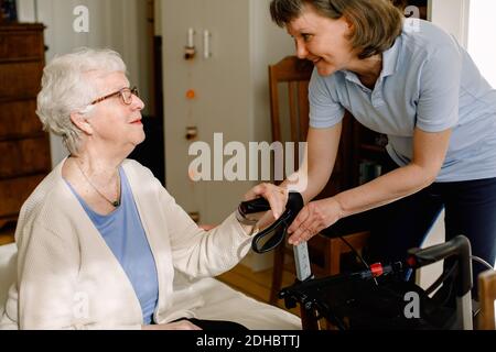 Smiling female healthcare worker looking at senior woman sitting with rollator in bedroom at nursing home Stock Photo