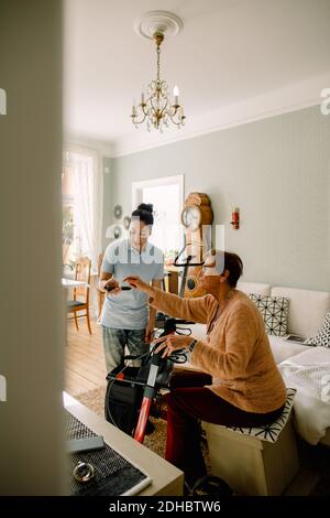 Young female social worker assisting senior woman in using remote control at nursing home Stock Photo