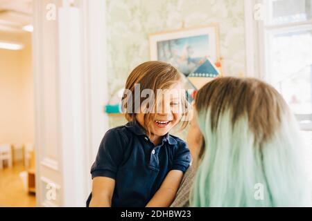 Smiling boy looking at dyed hair teacher in classroom Stock Photo