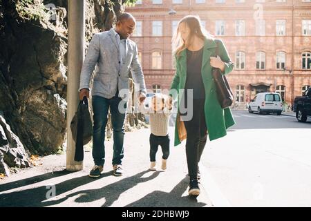 Full length of multi-ethnic parents holding daughter's hands while walking on footpath at city Stock Photo