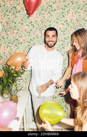 Portrait of smiling man standing with female friends and balloons at home during party Stock Photo