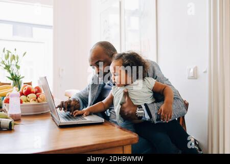 Father showing laptop to daughter while sitting at table in dining room Stock Photo