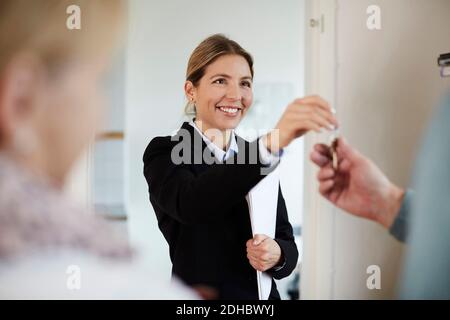 Confident smiling realtor giving house keys to couple Stock Photo