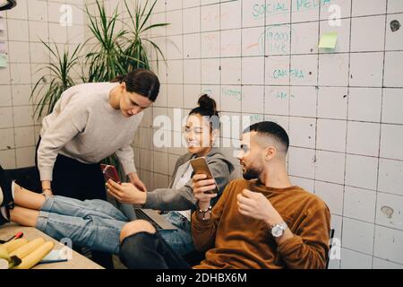 Young businesswoman sharing smart phone with colleagues while sitting at creative office Stock Photo