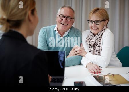 Happy senior couple talking to real estate agent in office