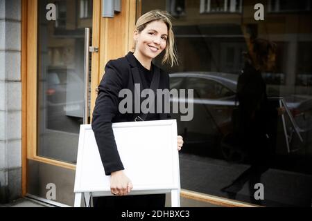 Portrait of smiling female real estate agent with blank signboard in city Stock Photo