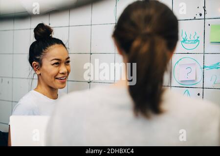 Smiling young female hackers discussing strategy over tile wall in creative office Stock Photo