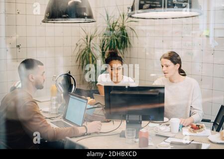 Young multi-ethnic computer programmers discussing at creative office seen through window Stock Photo