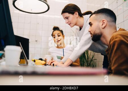 Young businesswoman using laptop while standing amidst colleagues at creative office Stock Photo