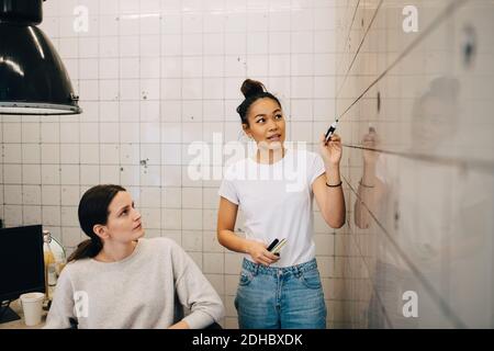 Young computer hacker explaining strategy to female colleague on tile wall at office Stock Photo