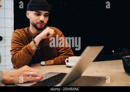 Young male hacker looking at female programmer using laptop at desk in office Stock Photo