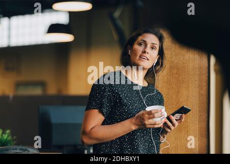 Female computer programmer with earphones talking on smart phone in creative office Stock Photo