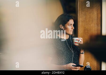 Thoughtful businesswoman drinking coffee while using mobile phone at office Stock Photo