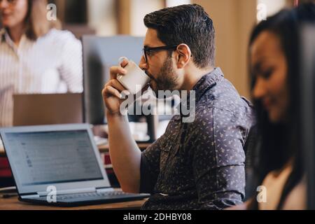 Mid adult businessman drinking coffee with laptop on desk in office Stock Photo