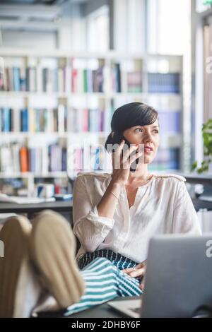 Creative businesswoman talking on mobile phone while relaxing at desk in office Stock Photo