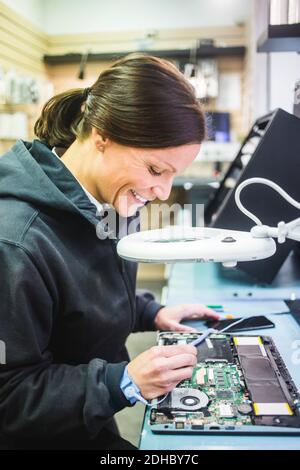 Side view of smiling mature technician working on computer part in workshop Stock Photo