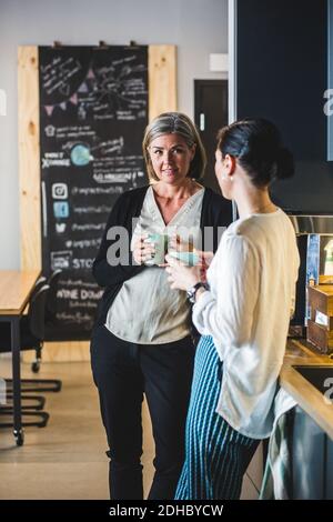 Female colleagues talking while having coffee at office cafeteria Stock Photo