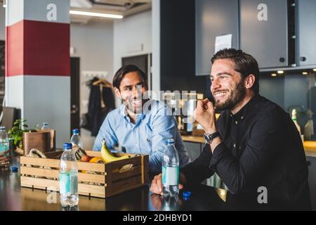 Male colleagues smiling while sitting at table in office Stock Photo