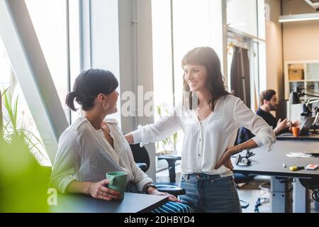 Female coworkers smiling while talking at counter in office Stock Photo
