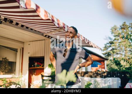 Happy young man looking away while standing with hands on hip at yard Stock Photo