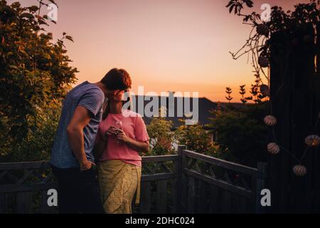 Couple kissing while standing at balcony during sunset Stock Photo