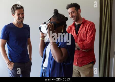 Businessmen smiling while looking at female colleague using virtual reality simulator in office Stock Photo