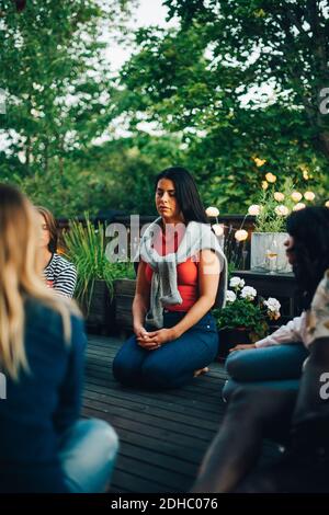 Mid adult woman sitting with eyes closed by friends in balcony during group session Stock Photo