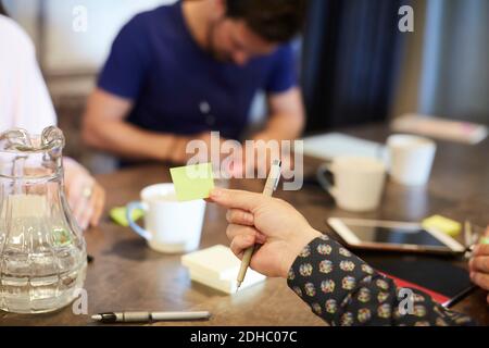 Cropped hand of businessman holding adhesive note during meeting in creative office Stock Photo