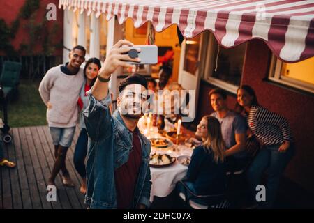 Smiling young man taking selfie with friends during dinner party Stock Photo