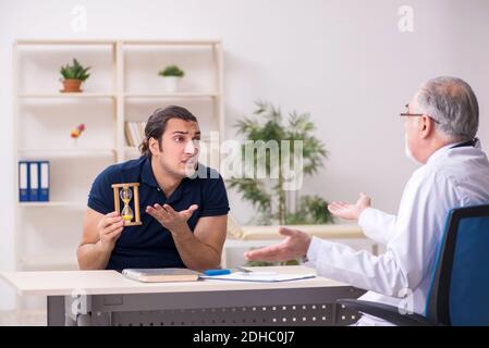Young male patient visiting old doctor in time management concep Stock Photo