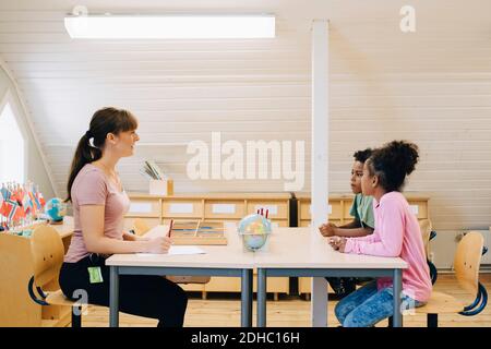 Teacher talking to school boys while sitting at desk in classroom Stock Photo