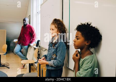 Male and female students standing against whiteboard at elementary school Stock Photo