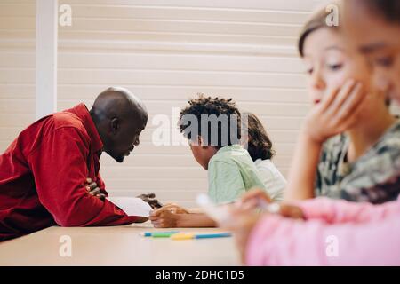 Teacher guiding students in learning through digital tablet at desk in classroom Stock Photo