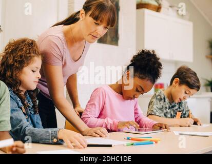 Teacher guiding male and female students at desk in classroom Stock Photo