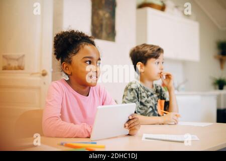 Boy learning through digital tablet while sitting with friend at classroom Stock Photo