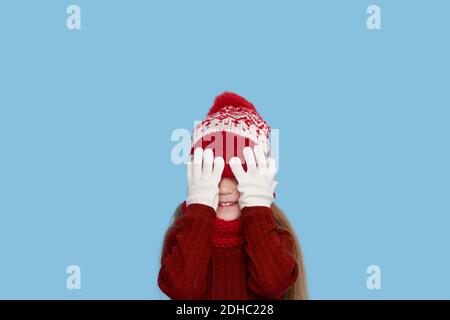 Winter portrait of happy child girl wearing knitted red hat, snood and sweater. Wow face. Blue background. childrens winter entertainment Stock Photo