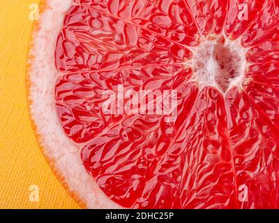 Slice of ripe juicy grapefruit on a yellow background macro shot. Ingredient for fruit desserts. Tasty vegetarian food, slimming diet and vitamins. Stock Photo