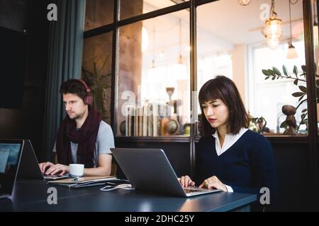 Confident female and male entrepreneurs using laptops at desk in office Stock Photo