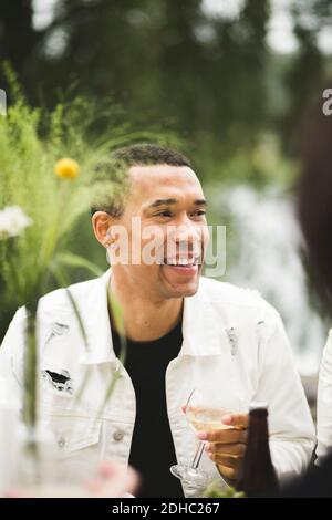 Smiling young man looking away while holding wineglass during dinner party Stock Photo