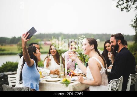 Cheerful young woman taking selfie with friends during dinner party in backyard Stock Photo