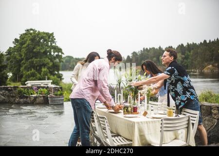 Multi-ethnic friends setting table for dinner party in backyard against clear sky Stock Photo